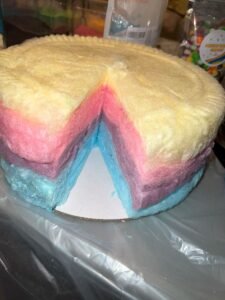 yellow, pink and blue layered round cotton candy cake with one slice missing